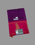 A folded Indian silk saree shown on a solid gray background. The saree features a deep purple upper body transitioning into a vibrant magenta-pink lower body with gold zari embroidery of a peacock and a red border.