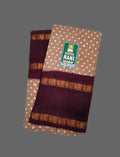 A folded Heritage Rani Handloom cotton fabric piece, likely a sari, in brown with white polka dots, deep maroon borders, and gold zari motifs, displayed on a solid gray background.